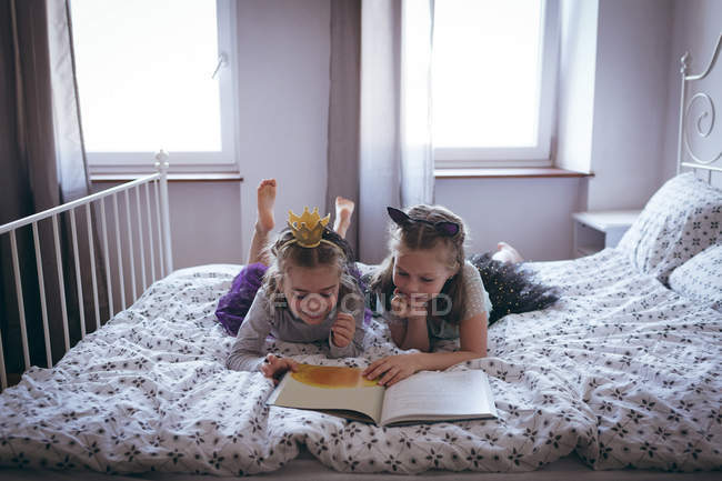 Sœurs lisant un livre sur le lit dans la chambre — Photo de stock