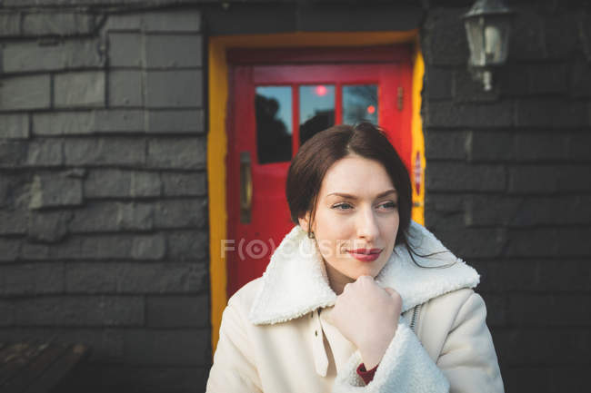 Nachdenkliche Frau in warmer Kleidung steht vor Haus. — Stockfoto