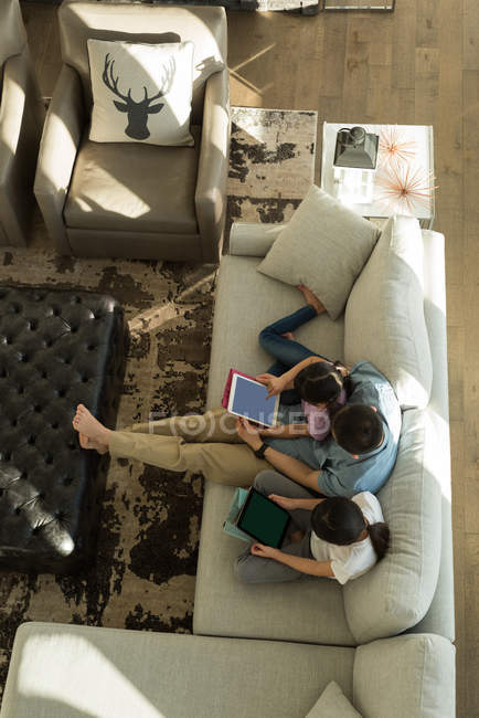 Vue aérienne des filles utilisant une tablette numérique avec son père dans le salon à la maison — Photo de stock