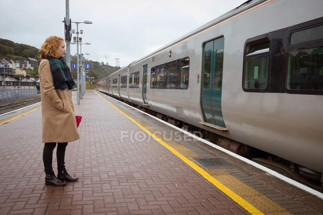 Jovem mulher de pé na plataforma em frente ao trem em um dia chuvoso — Fotografia de Stock