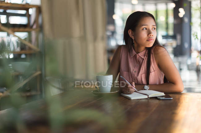 Nachdenkliches Teenager-Mädchen schreibt im Restaurant an einem Tagebuch — Stockfoto