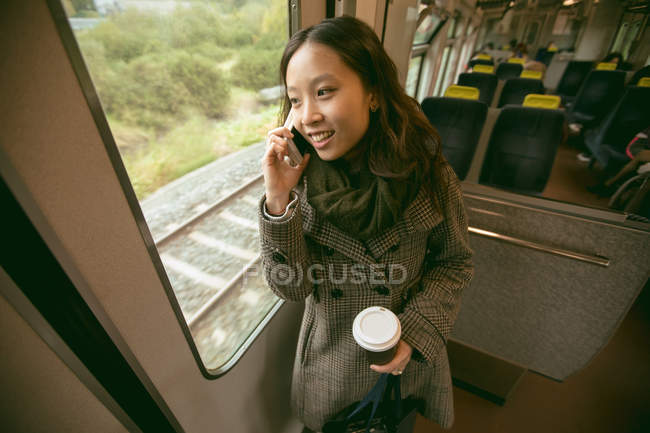 Счастливая женщина разговаривает по мобильному телефону во время поездки на поезде — стоковое фото