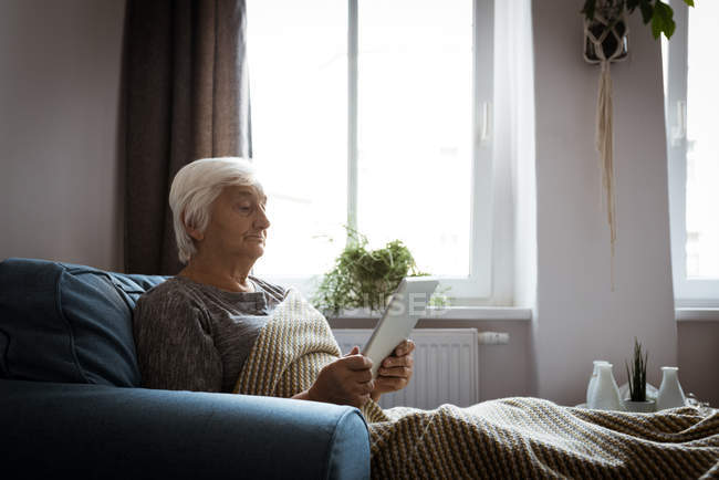 Mujer mayor usando tableta en la sala de estar en casa - foto de stock