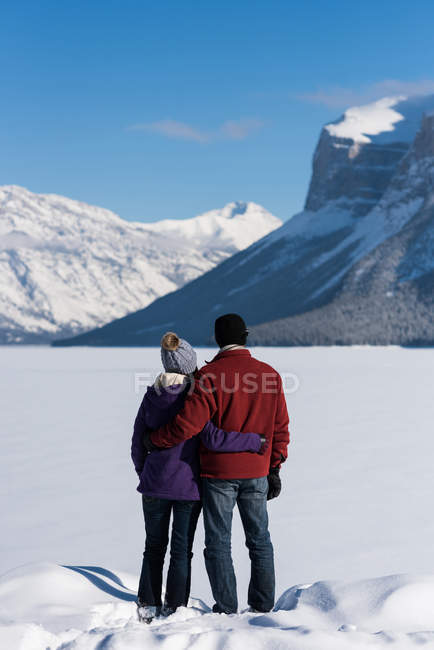 Rear view of couple standing with arm around in snowy landscape. — Stock Photo