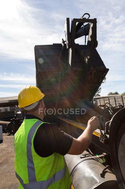 Close-up do trabalhador levantando o recipiente de um caminhão basculante — Fotografia de Stock