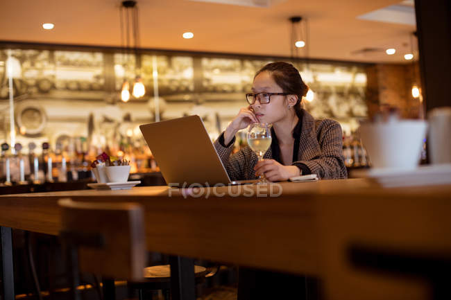 Femme exécutive utilisant un ordinateur portable tout en ayant du vin à l'hôtel — Photo de stock