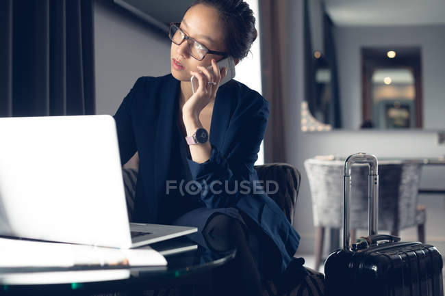 Woman talking on mobile phone while using laptop at table — Stock Photo
