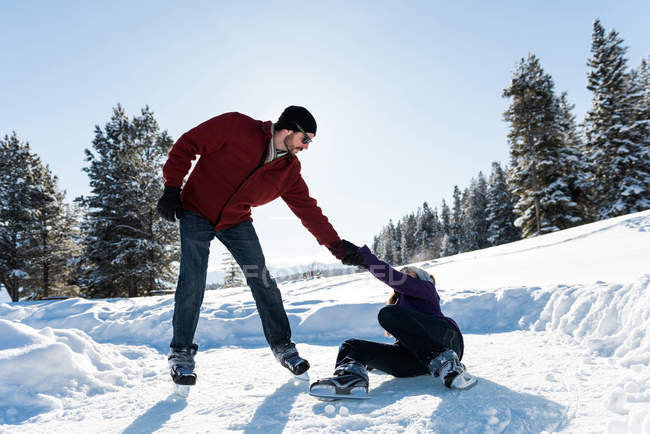 Homem ajudando mulher levantando-se enquanto patinava na paisagem nevada . — Fotografia de Stock