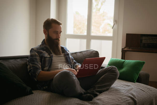 Hombre usando el portátil en el sofá en la sala de estar - foto de stock