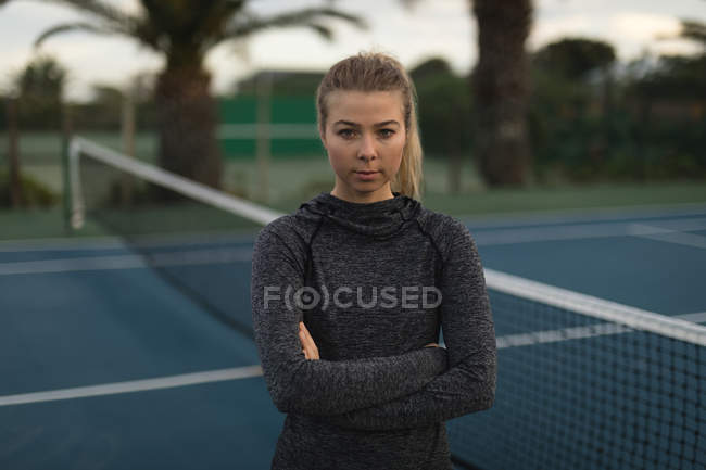 Portrait of woman standing with arms crossed in tennis court — Stock Photo
