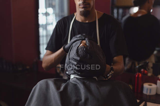 Barbeiro limpando o rosto dos clientes com toalha na barbearia — Fotografia de Stock