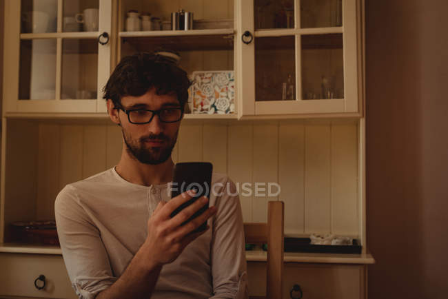 Uomo che utilizza il telefono cellulare in cucina a casa — Foto stock