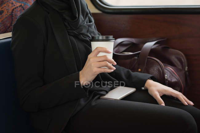 Partie médiane de la femme dans le hijab prendre un café tout en voyageant en train — Photo de stock