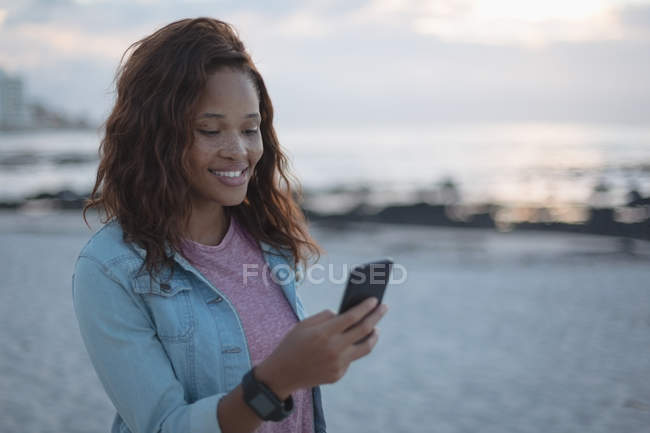 Молода жінка використовує мобільний телефон на пляжі — стокове фото