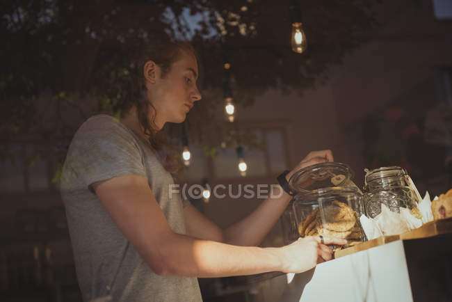 Waiter looking at cookies in jar at counter of cafeteria — Stock Photo