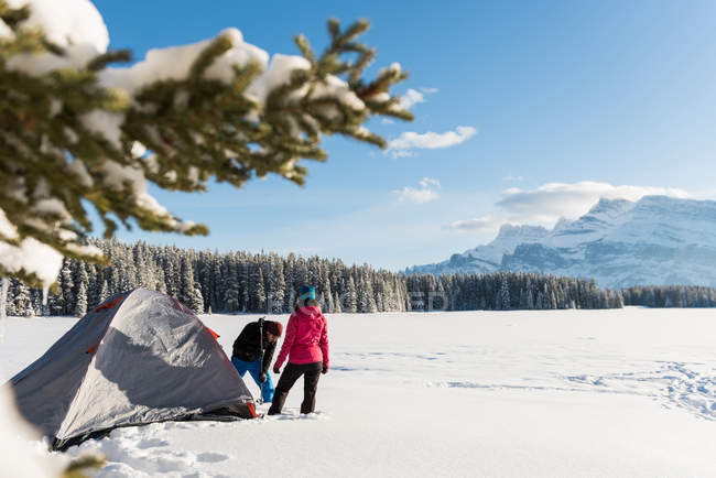 Paar schlägt im Winter sein Zelt in verschneiter Landschaft auf. — Stockfoto