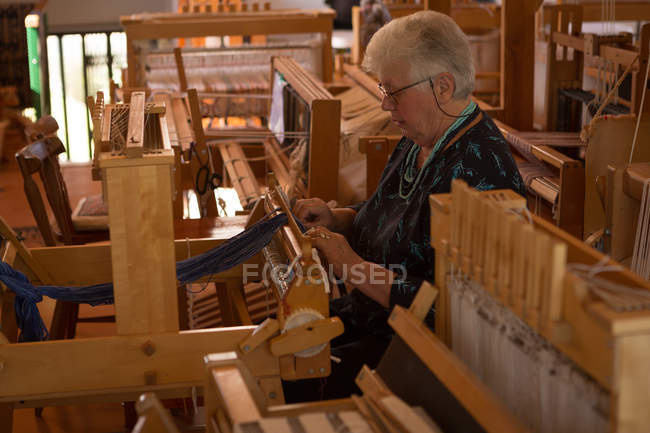 Active senior woman weaving silk at shop — Stock Photo