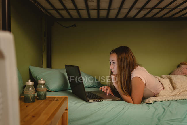 Девушка лежит на двухъярусной кровати и использует ноутбук в спальне . — стоковое фото