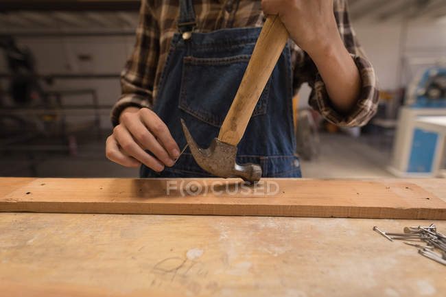 Mittelteil der Handwerkerin mit Hammer auf Holz in Werkstatt. — Stockfoto
