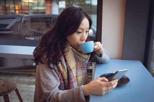 Mulher bonita usando telefone celular enquanto toma café na cafetaria — Fotografia de Stock
