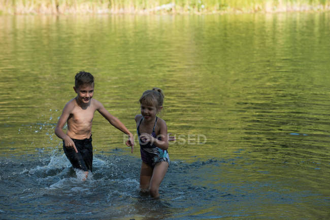 Братья и сёстры играют в реке в солнечный день — стоковое фото