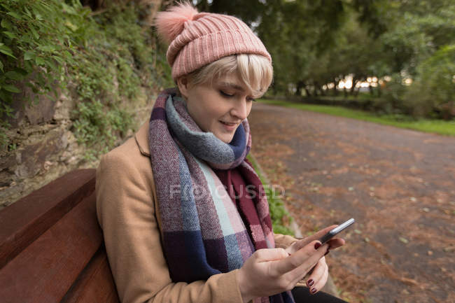 Woman in warm clothing using mobile phone in park — Stock Photo