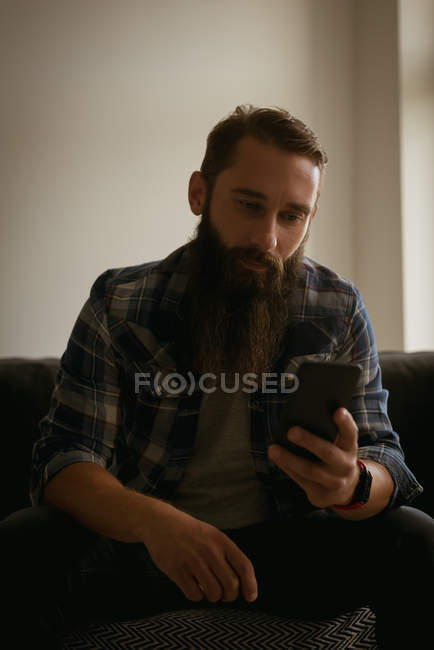 Чоловік використовує мобільний телефон на дивані у вітальні — стокове фото
