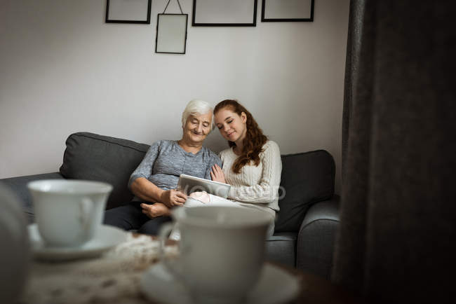 Бабушка и внучка используют цифровые планшеты в гостиной дома — стоковое фото