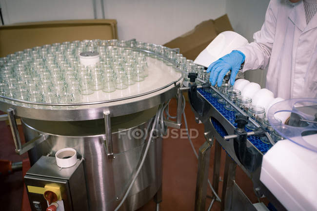 Section médiane du travailleur féminin surveillant les bocaux en verre sur la chaîne de production — Photo de stock