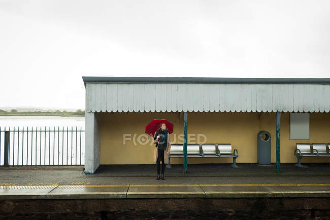 Jovem mulher de pé com guarda-chuva na estação ferroviária — Fotografia de Stock