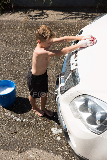 Niño lavando un coche en el garaje exterior en un día soleado - foto de stock