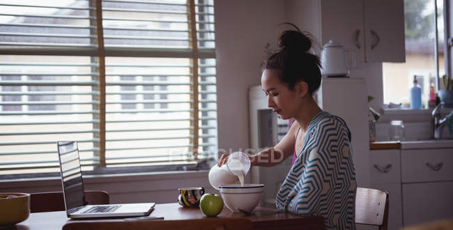 Femme versant du lait dans un bol à la maison — Photo de stock