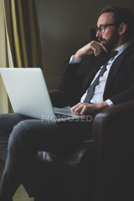 Pensativo hombre de negocios utilizando el ordenador portátil en la habitación de hotel - foto de stock