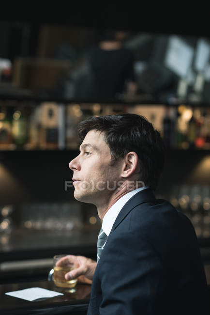 Pensativo hombre de negocios tomando un vaso de whisky en el mostrador del hotel - foto de stock