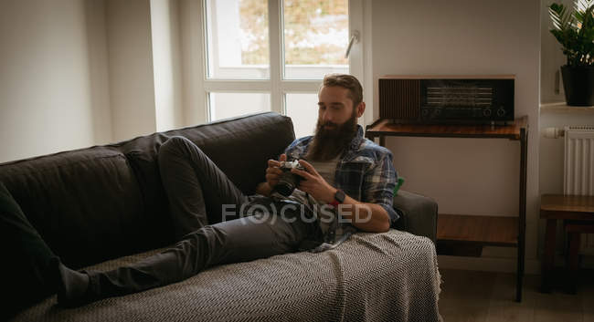 Человек рассматривает изображение на цифровой камере, расслабляясь на диване — стоковое фото