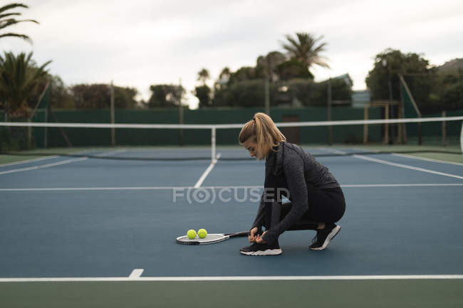 Giovane donna legando i lacci delle scarpe nel campo da tennis — Foto stock