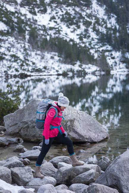 Woman with backpack walking at lakeside during winter — Stock Photo