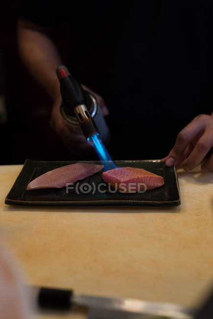 Chef cuisinier tranche de poisson avec une torche soufflée dans un restaurant — Photo de stock