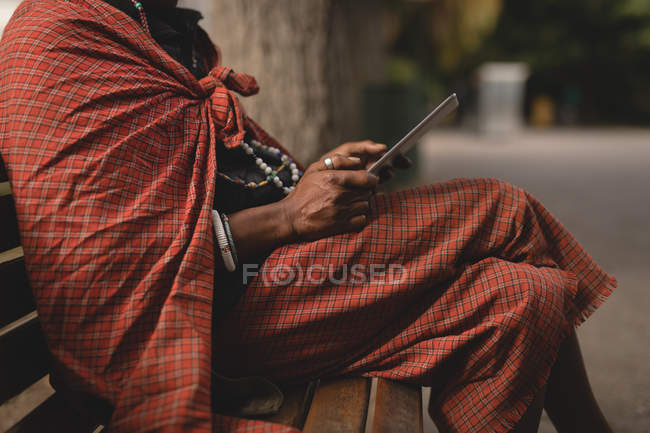 Sección media del hombre maasai en ropa tradicional usando teléfono móvil - foto de stock