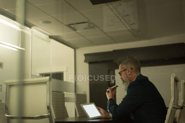 Бизнес-руководитель разговаривает по мобильному телефону при использовании цифрового планшета в офисе — стоковое фото