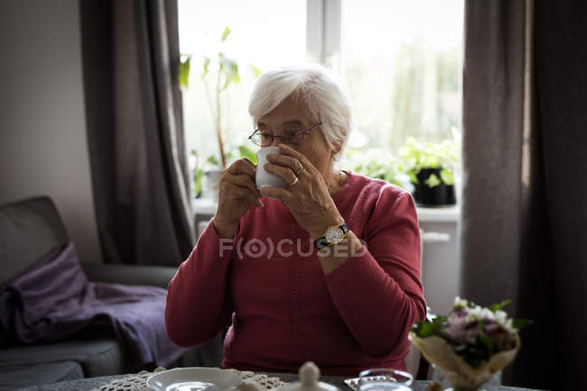 Mujer mayor tomando una taza de té en la sala de estar en casa - foto de stock