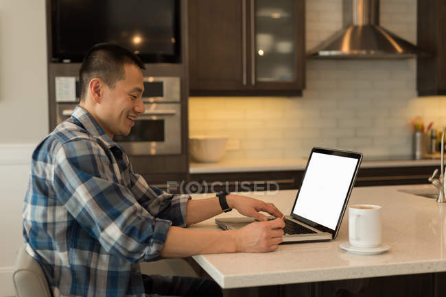 Homme utilisant un ordinateur portable dans la cuisine à la maison — Photo de stock