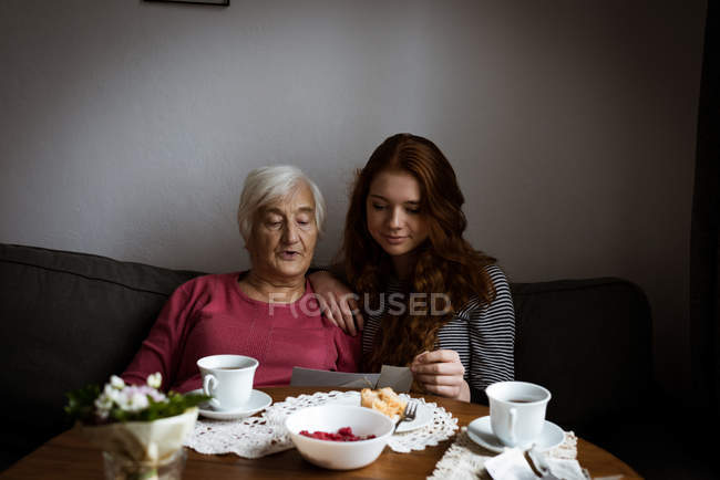Grandmother and granddaughter looking at photograph in living room — Stock Photo