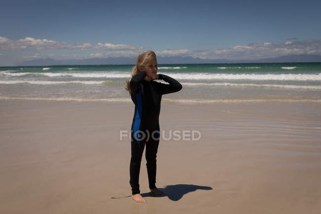 Задумчивая девушка в гидрокостюме стоит на пляже — стоковое фото