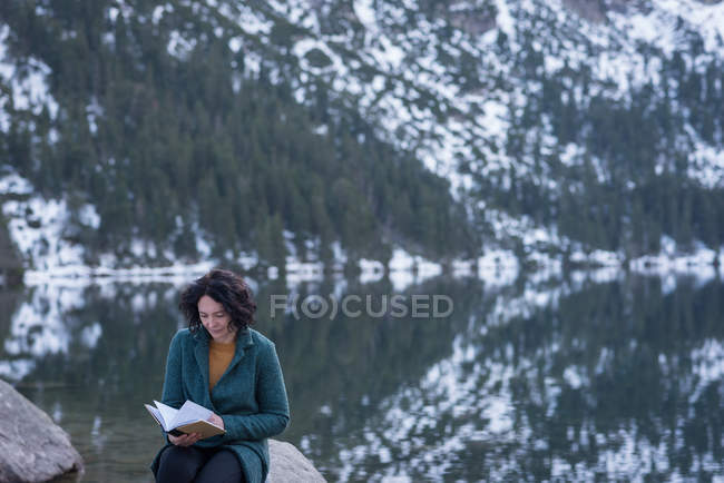 Frau liest im Winter am Seeufer Buch — Stockfoto