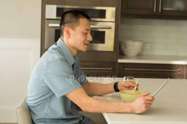 Uomo che utilizza tablet digitale mentre fa colazione a casa — Foto stock