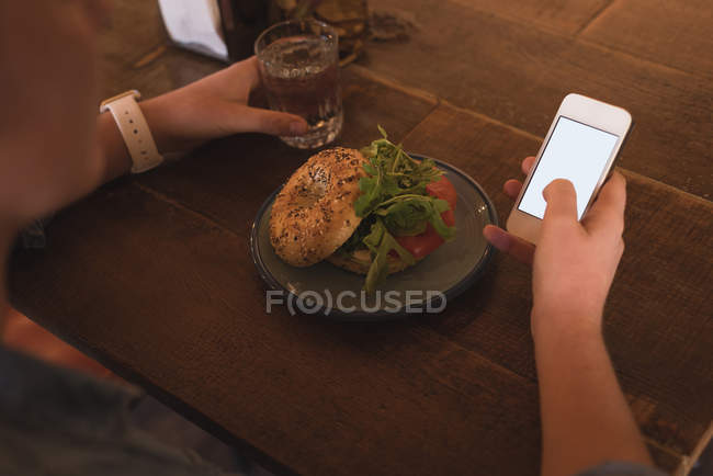 Mid section of woman using mobile while having breakfast at table in cafe — Stock Photo