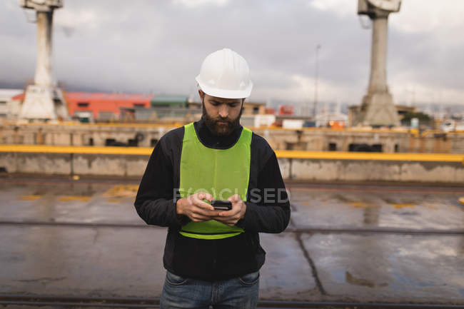 Trabajador portuario usando teléfono móvil en astillero - foto de stock