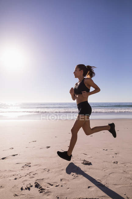Mujer en forma corriendo en la playa de arena al atardecer . - foto de stock