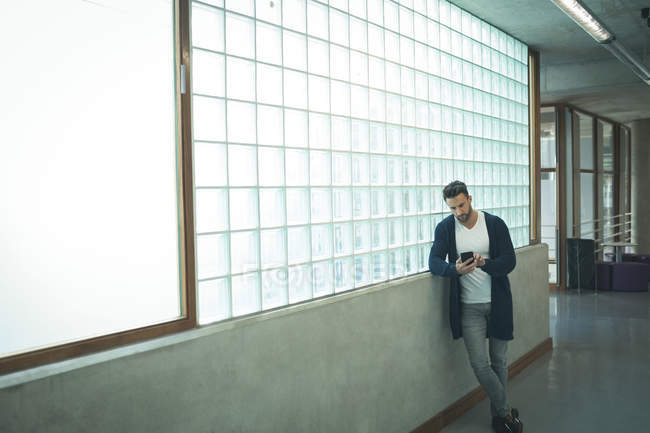 Чоловік виконавчий використовує мобільний телефон в офісному коридорі — стокове фото